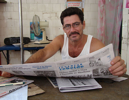 A man with glasses reads a newspaper in Cuba